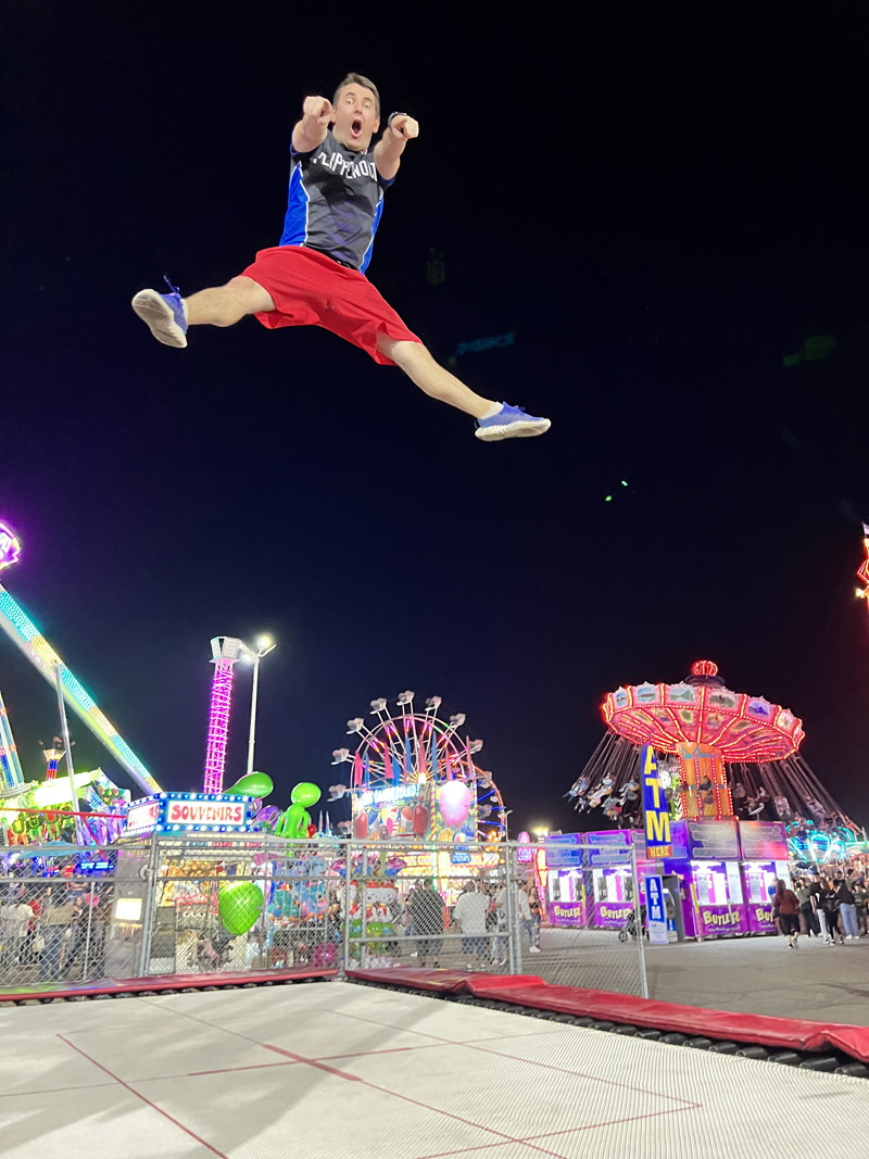 athlete in air jumping on trampoline outside at a fair