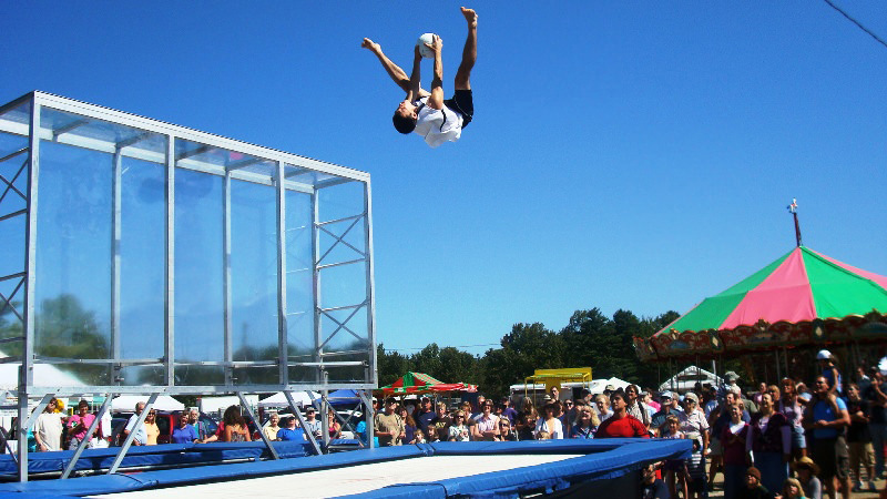 athlete in air jumping on trampoline holding a ball outside